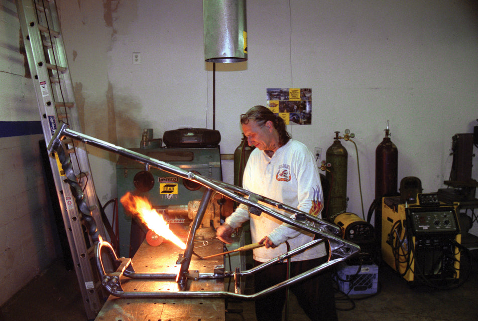Indian Larry lighting a torch next to a twisted down tube frame
